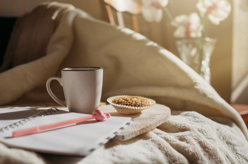 notepad, pen, coffee, and muffin on a bed; morning routine for busy moms